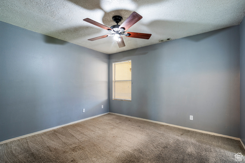 Carpeted empty room featuring ceiling fan and a textured ceiling