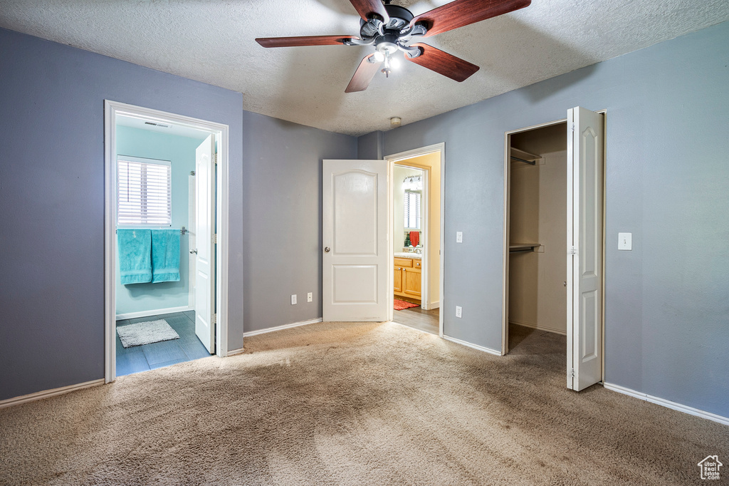 Unfurnished bedroom with ceiling fan, a textured ceiling, carpet, a walk in closet, and ensuite bathroom