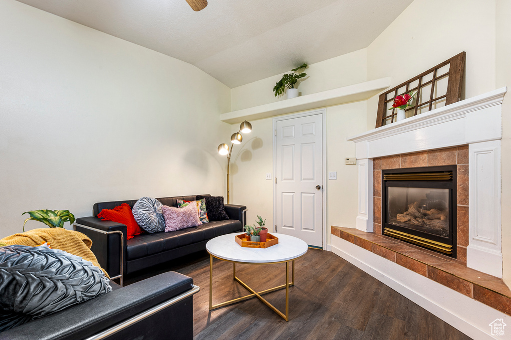 Living room with vaulted ceiling, a tiled fireplace, and dark wood-type flooring