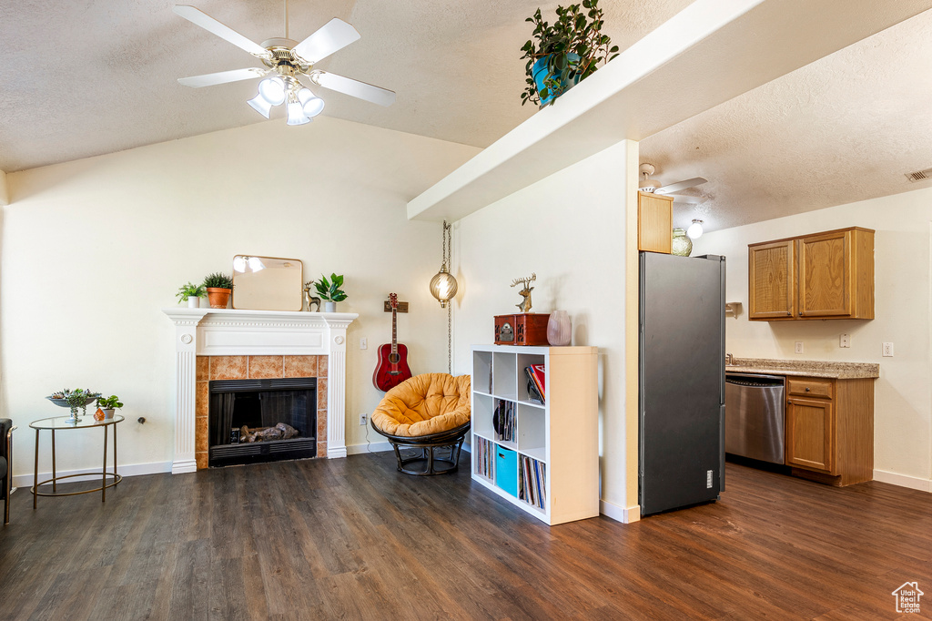 Living area with ceiling fan, a textured ceiling, dark hardwood / wood-style floors, a tile fireplace, and vaulted ceiling