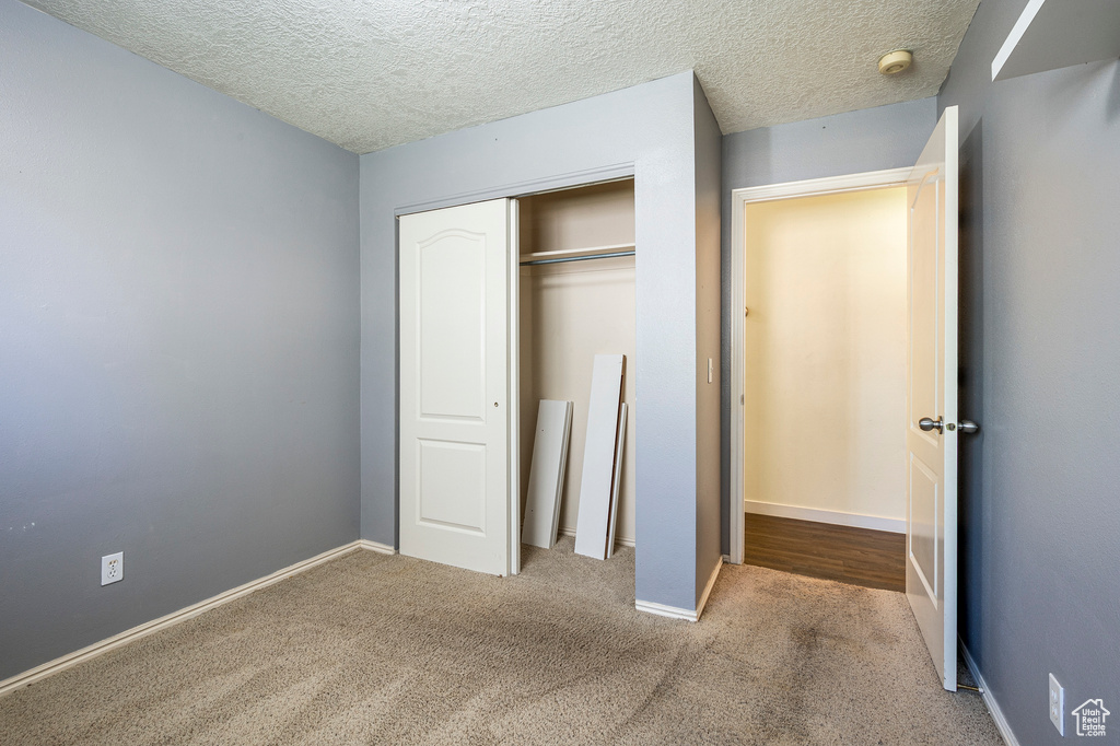 Unfurnished bedroom with light carpet, a closet, and a textured ceiling