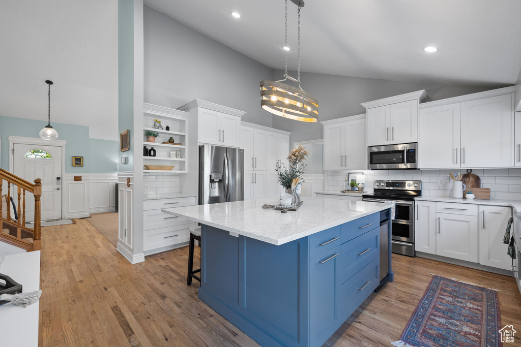 Kitchen with pendant lighting, stainless steel appliances, high vaulted ceiling, a center island, and white cabinetry