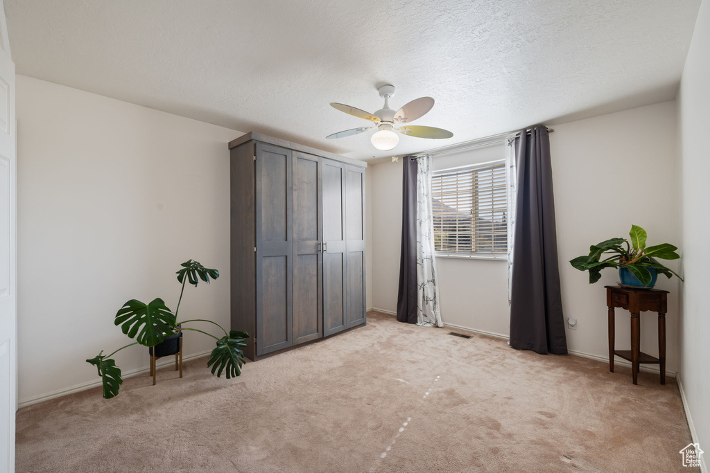 Carpeted bedroom featuring ceiling fan, a textured ceiling, and a closet