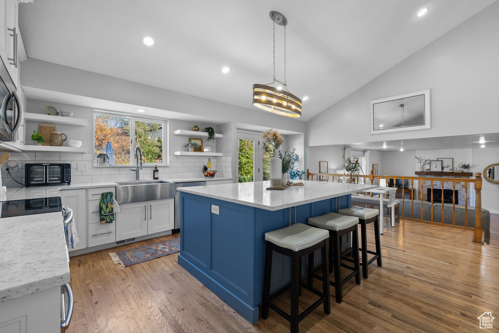 Kitchen with light wood-type flooring, decorative light fixtures, sink, white cabinets, and a center island