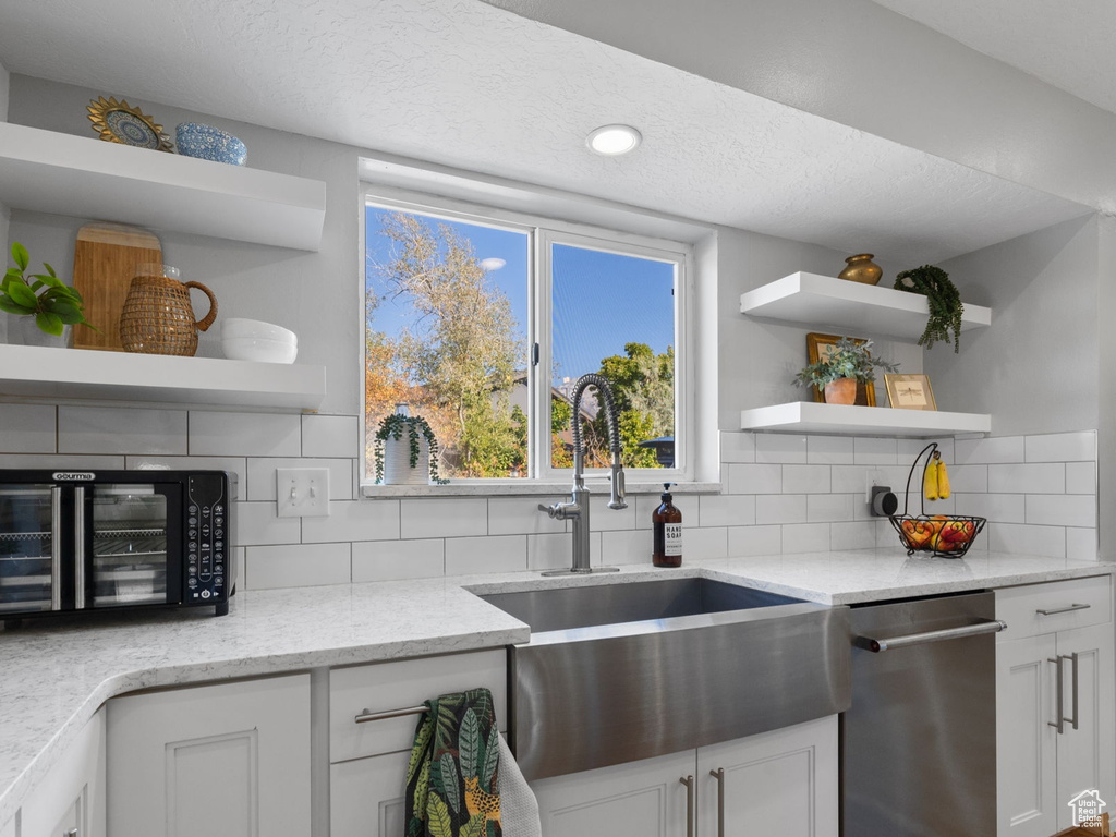 Kitchen featuring light stone countertops, stainless steel dishwasher, sink, white cabinetry, and backsplash