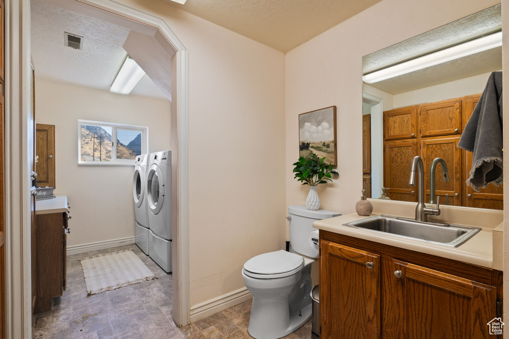 Bathroom with a textured ceiling, washing machine and dryer, vanity, and toilet