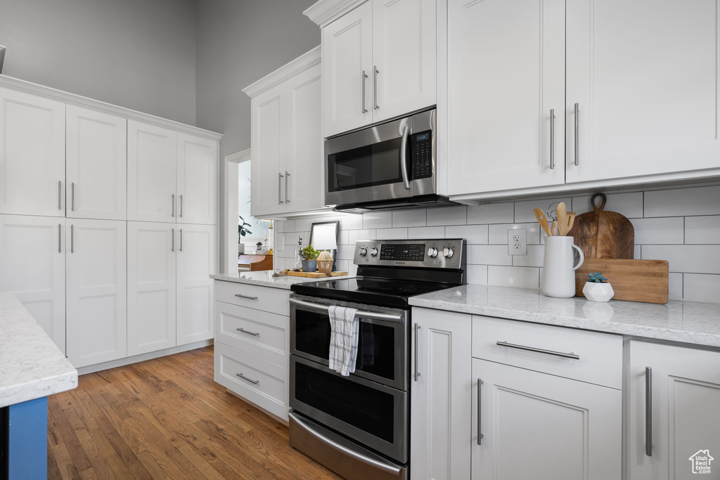 Kitchen featuring light stone countertops, dark wood-type flooring, stainless steel appliances, and white cabinets