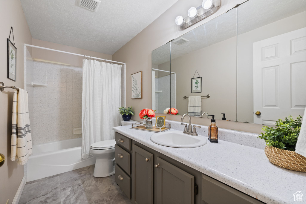 Full bathroom featuring shower / bath combo, toilet, vanity, and a textured ceiling