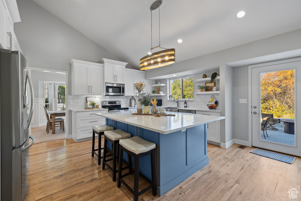 Kitchen with light wood-type flooring, a kitchen island, hanging light fixtures, appliances with stainless steel finishes, and white cabinetry