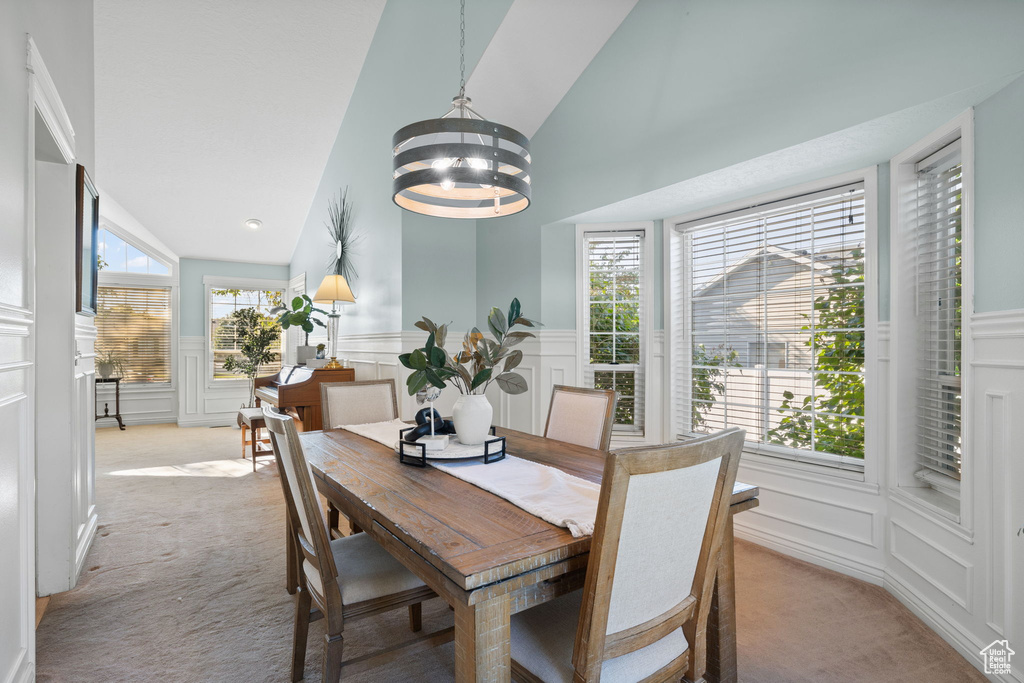 Carpeted dining room featuring a chandelier, high vaulted ceiling, and a healthy amount of sunlight