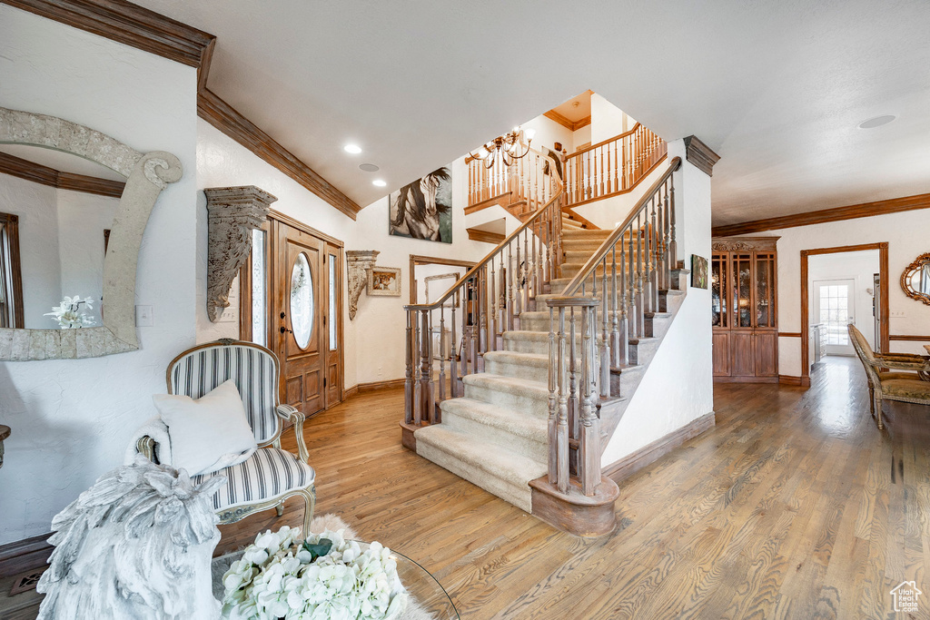 Stairway with crown molding, an inviting chandelier, baseboards, wood finished floors, and vaulted ceiling