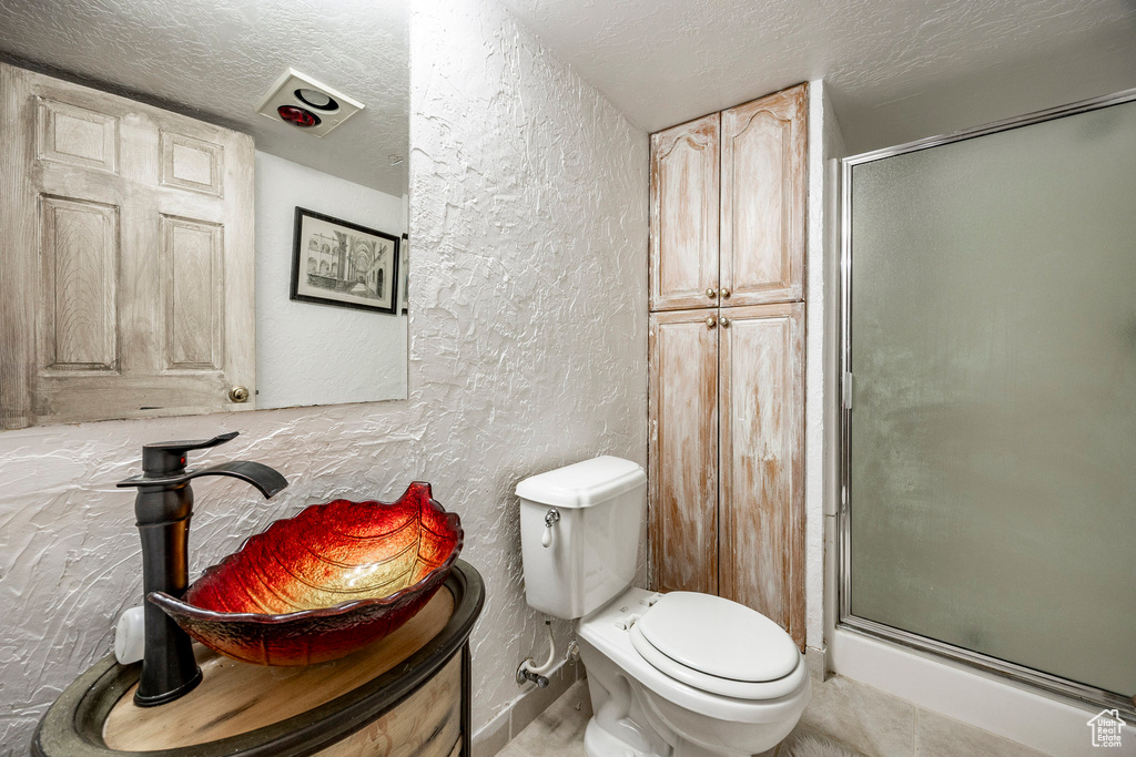 Full bath featuring a textured wall, a shower stall, toilet, and a textured ceiling