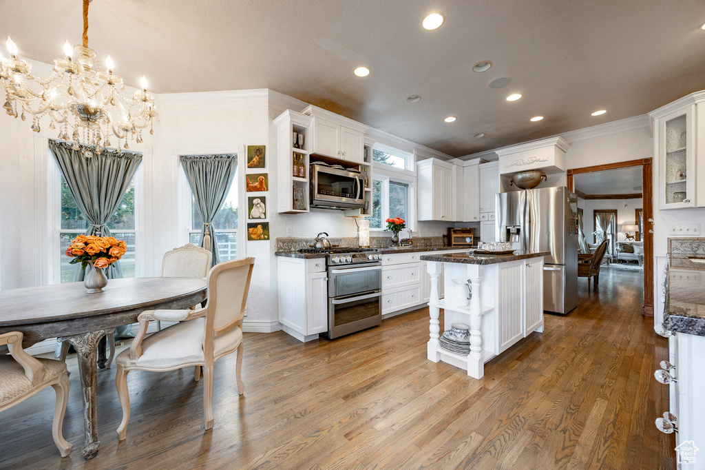 Kitchen with open shelves, ornamental molding, white cabinets, a notable chandelier, and stainless steel appliances