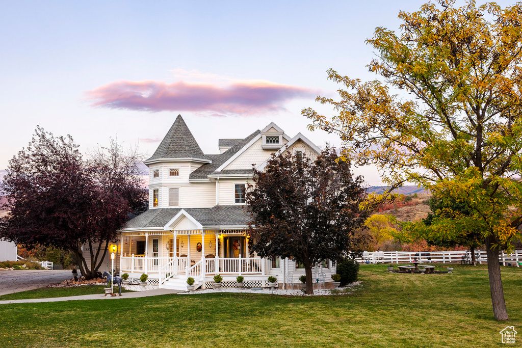 Victorian home featuring a shingled roof, fence, covered porch, and a front yard