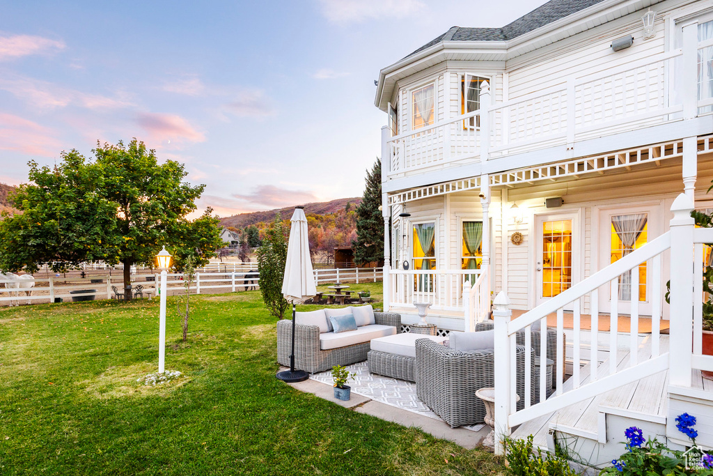 Yard at dusk featuring fence, an outdoor hangout area, a mountain view, a patio area, and a balcony