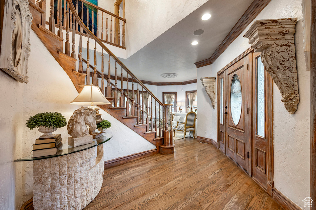 Foyer with stairs, a textured wall, ornamental molding, and wood finished floors