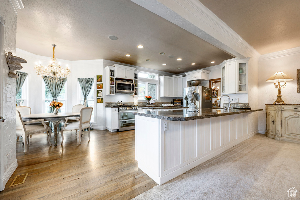 Kitchen with crown molding, open shelves, an inviting chandelier, a peninsula, and appliances with stainless steel finishes