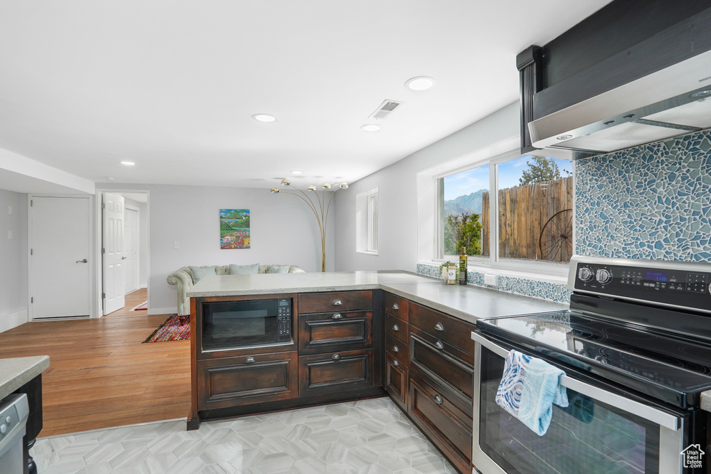 Kitchen with wall chimney exhaust hood, light hardwood / wood-style floors, kitchen peninsula, black microwave, and electric range