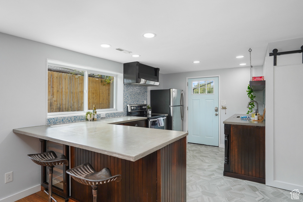 Kitchen with stainless steel appliances, kitchen peninsula, a barn door, a kitchen breakfast bar, and backsplash