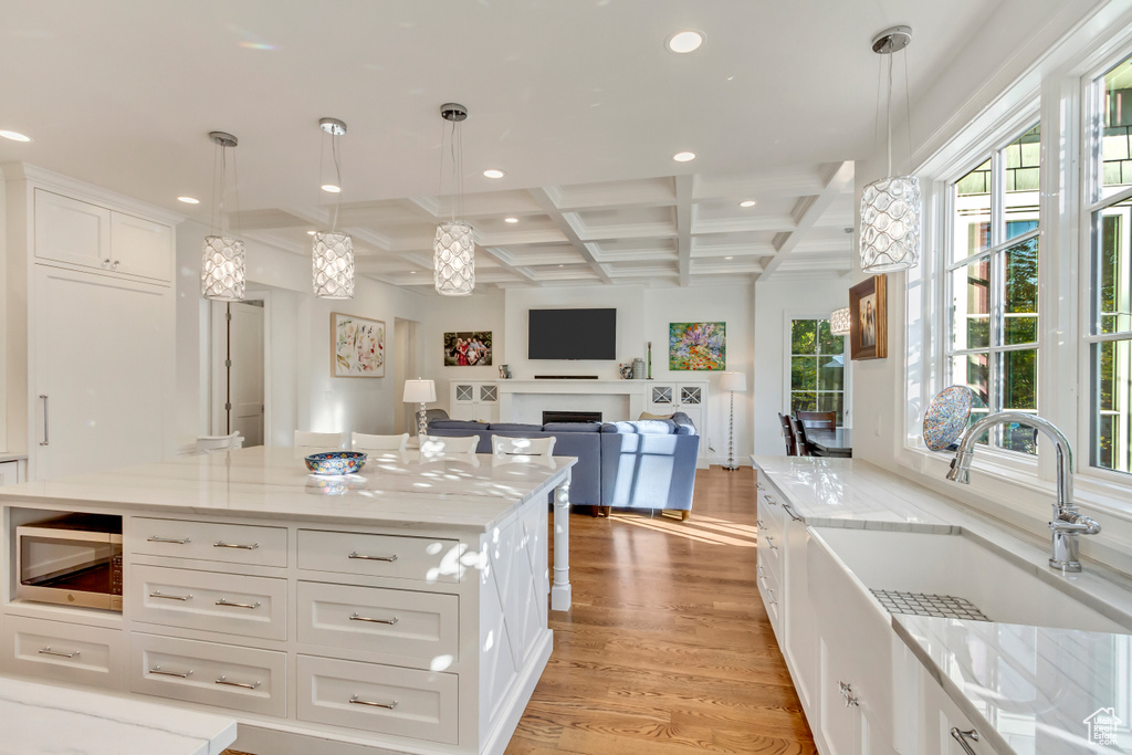 Kitchen with coffered ceiling, white cabinets, light wood-type flooring, and hanging light fixtures