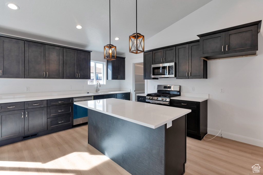 Kitchen featuring a center island, light hardwood / wood-style floors, pendant lighting, vaulted ceiling, and appliances with stainless steel finishes