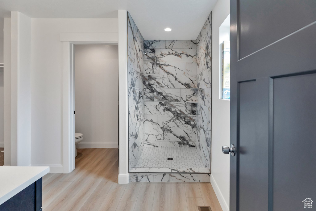 Bathroom with a tile shower, hardwood / wood-style floors, vanity, and toilet