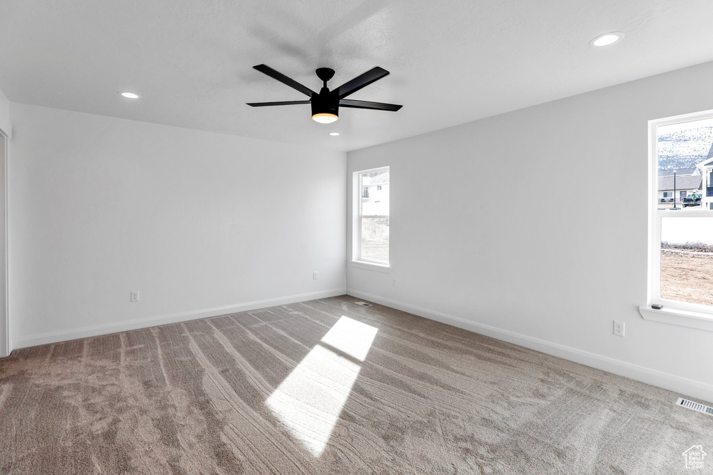 Carpeted empty room with ceiling fan and a wealth of natural light