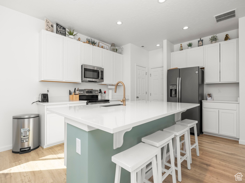 Kitchen with light hardwood / wood-style floors, a kitchen island with sink, a kitchen breakfast bar, stainless steel appliances, and white cabinets