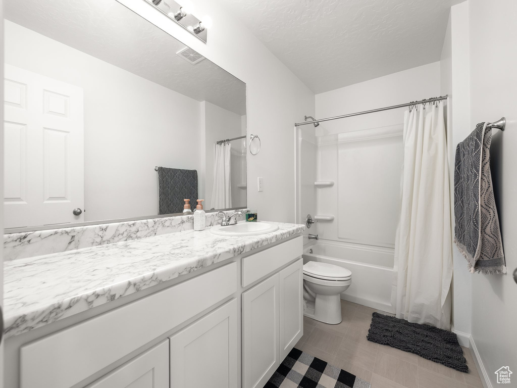 Full bathroom featuring shower / bath combination with curtain, vanity, toilet, and a textured ceiling