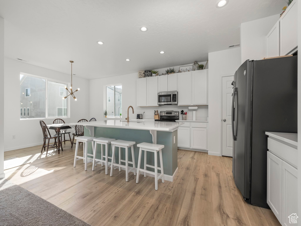 Kitchen featuring hanging light fixtures, white cabinets, appliances with stainless steel finishes, and light wood-type flooring