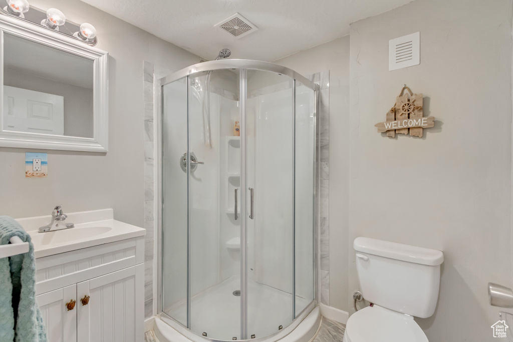 Bathroom with a shower with shower door, vanity, and toilet