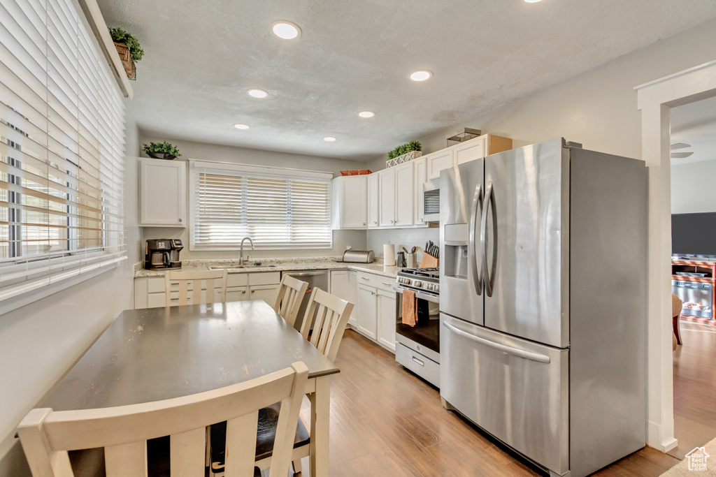 Kitchen featuring white cabinets, stainless steel appliances, light wood-type flooring, and sink