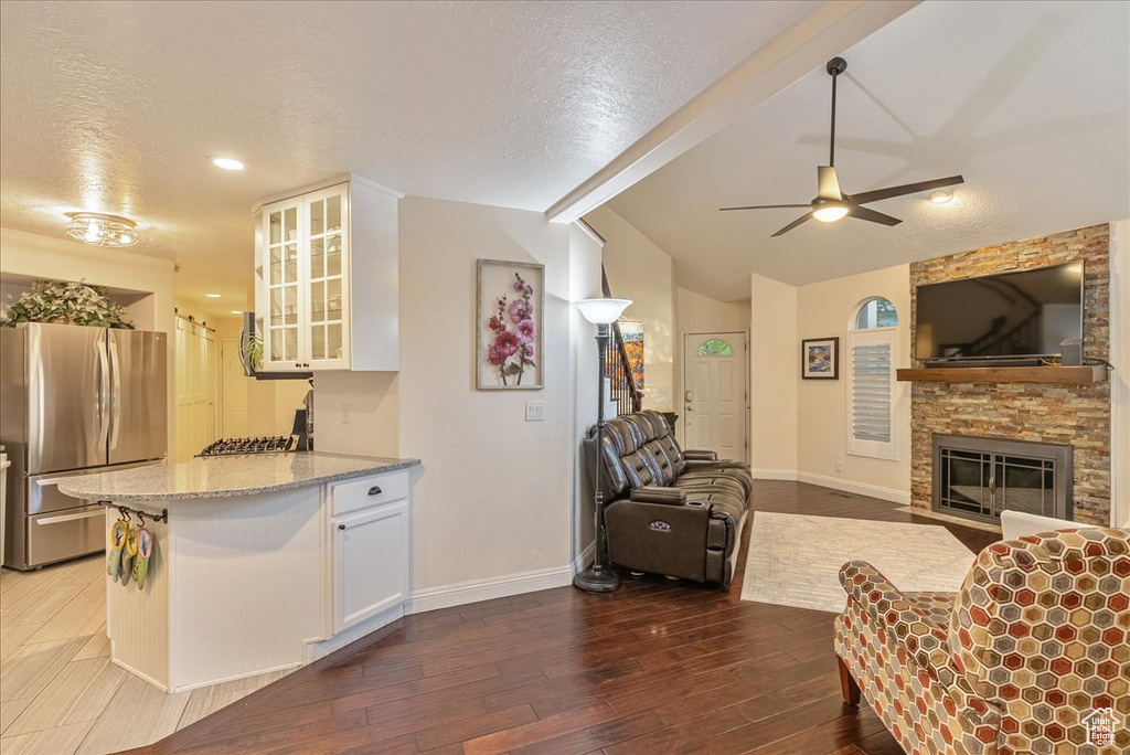 Living room featuring dark wood-type flooring, vaulted ceiling with beams, a fireplace, and a textured ceiling