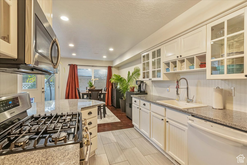 Kitchen featuring light stone counters, sink, white cabinetry, stainless steel appliances, and light hardwood / wood-style floors