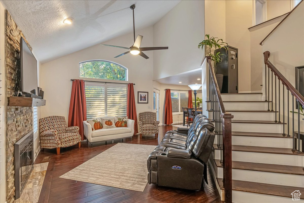 Living room featuring ceiling fan, a fireplace, dark hardwood / wood-style floors, high vaulted ceiling, and a textured ceiling