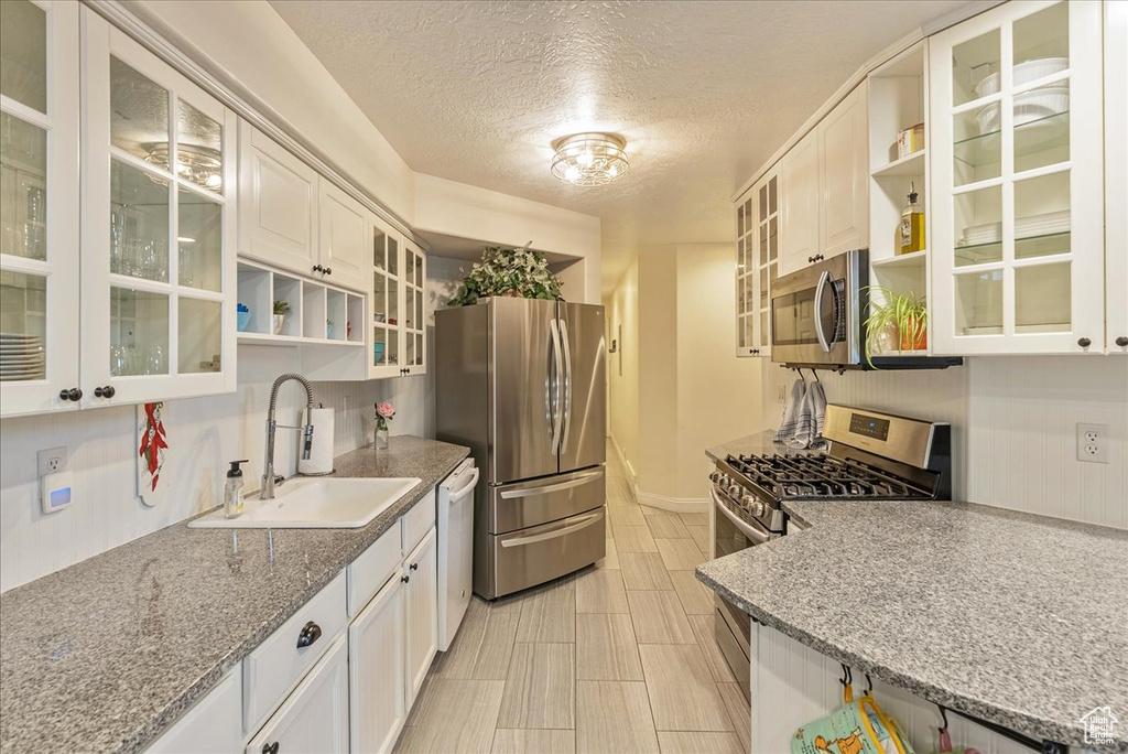 Kitchen featuring light stone counters, white cabinets, sink, a textured ceiling, and appliances with stainless steel finishes