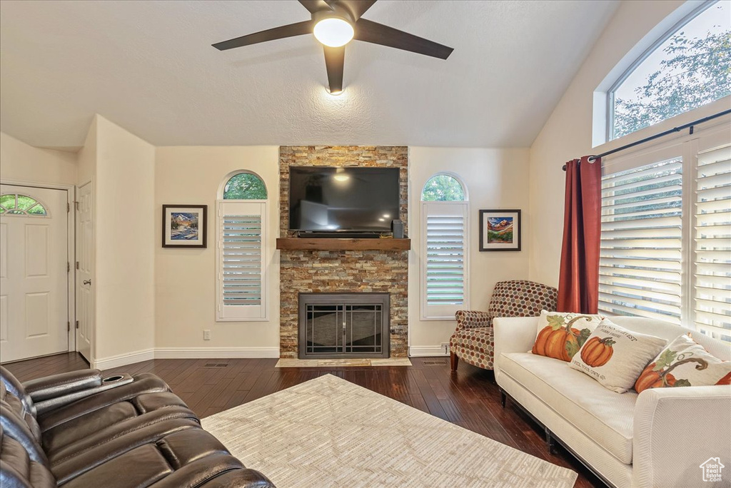 Living room featuring ceiling fan, vaulted ceiling, a fireplace, and dark wood-type flooring