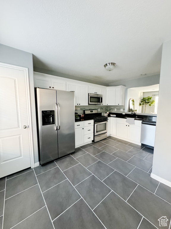 Kitchen featuring dark tile patterned floors, white cabinets, stainless steel appliances, and tasteful backsplash