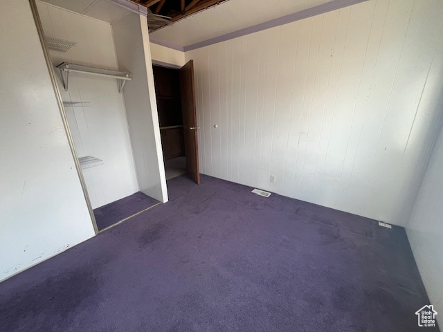 Unfurnished bedroom with wood walls, a closet, and dark carpet