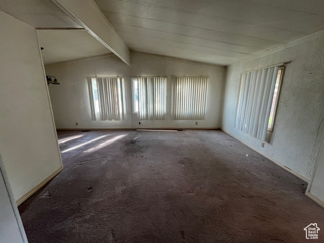 Carpeted empty room featuring lofted ceiling with beams and a healthy amount of sunlight