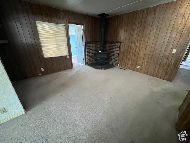 Unfurnished living room featuring wood walls, light colored carpet, and a wood stove