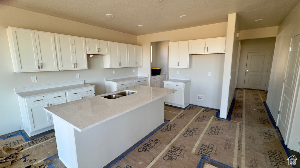 Kitchen featuring white cabinetry, a textured ceiling, sink, and a center island with sink