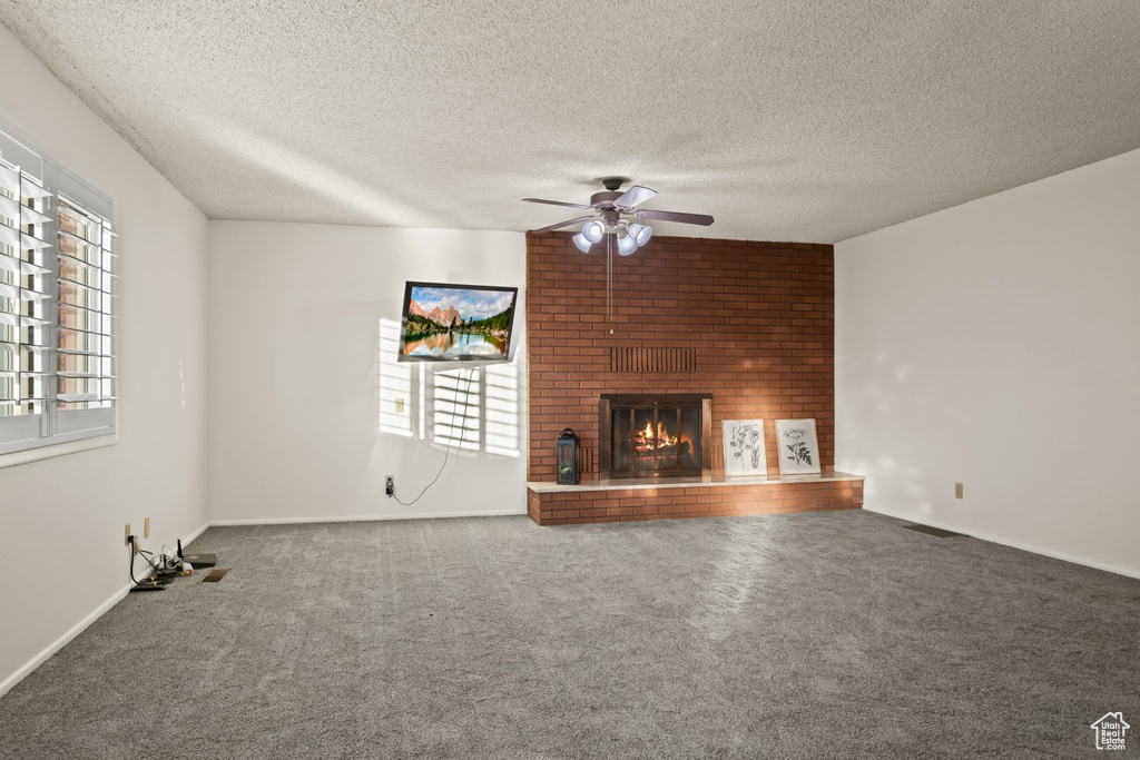 Unfurnished living room featuring ceiling fan, a textured ceiling, a fireplace, and carpet flooring