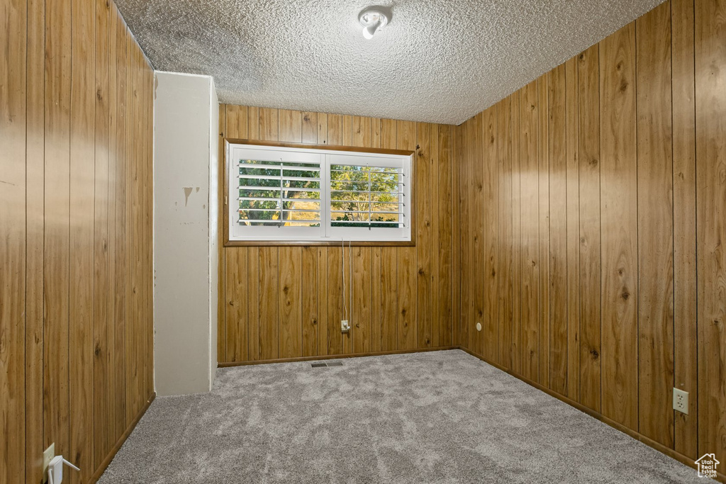 Spare room with a textured ceiling, wooden walls, and light carpet