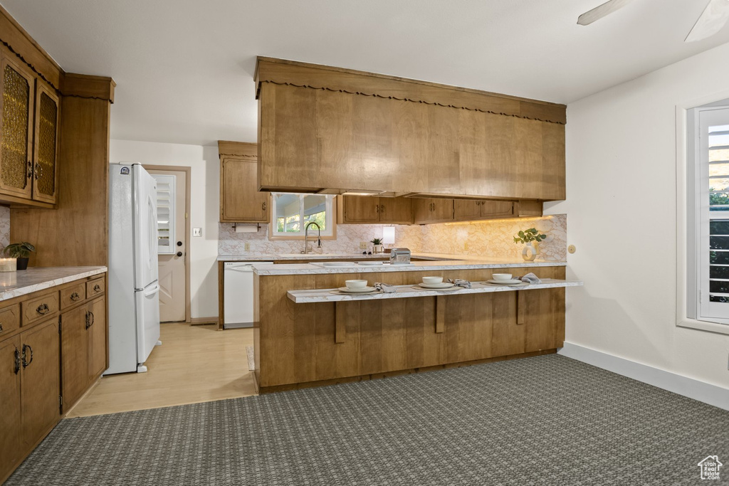 Kitchen featuring kitchen peninsula, white appliances, a kitchen breakfast bar, and tasteful backsplash