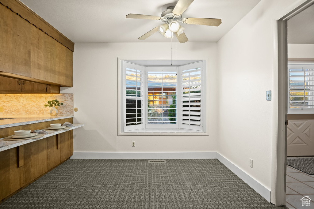 Dining space featuring ceiling fan, plenty of natural light, and dark colored carpet