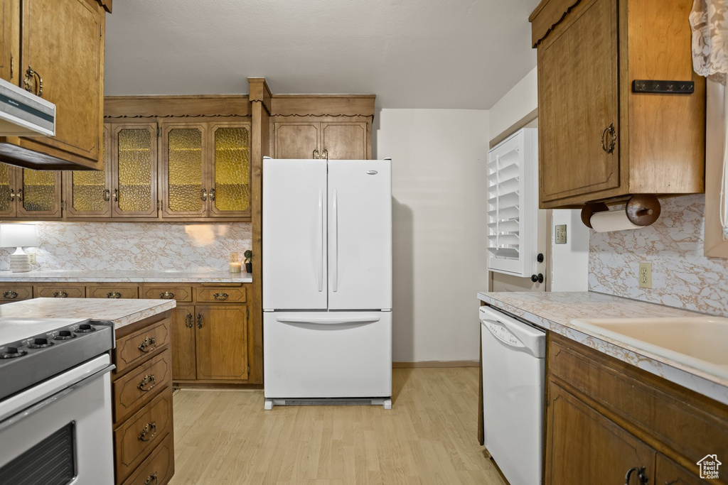 Kitchen featuring light hardwood / wood-style flooring, tasteful backsplash, white appliances, and extractor fan