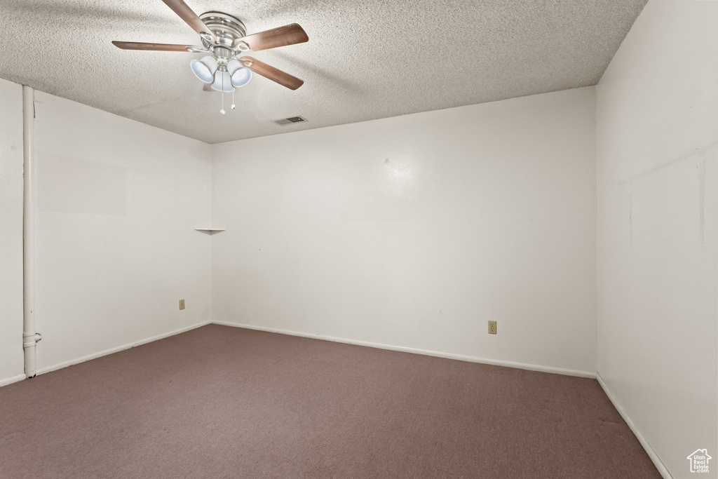 Unfurnished room featuring ceiling fan, dark carpet, and a textured ceiling