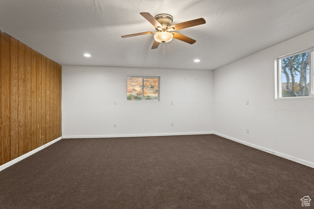 Carpeted empty room featuring wooden walls, ceiling fan, and a textured ceiling