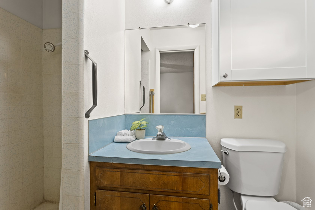 Bathroom featuring a tile shower, vanity, and toilet